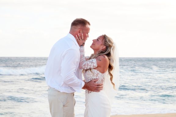Sandy Beach Wedding Ceremony A couple in wedding attire shares a loving moment on a beach.
