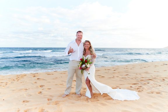 Sandy Beach Wedding Ceremony A happy couple stands on a beach, dressed in wedding attire, holding flowers.