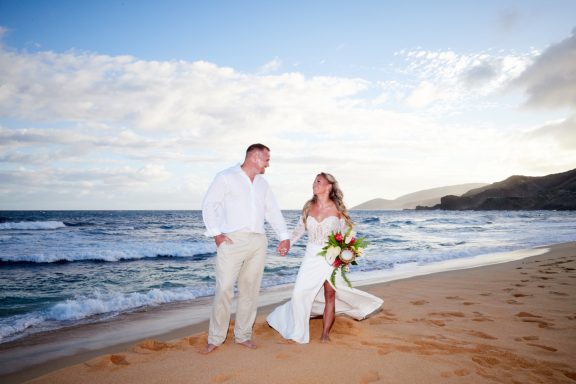 Sandy Beach Wedding Ceremony A couple in wedding attire walks hand in hand on a sandy beach by the ocean.