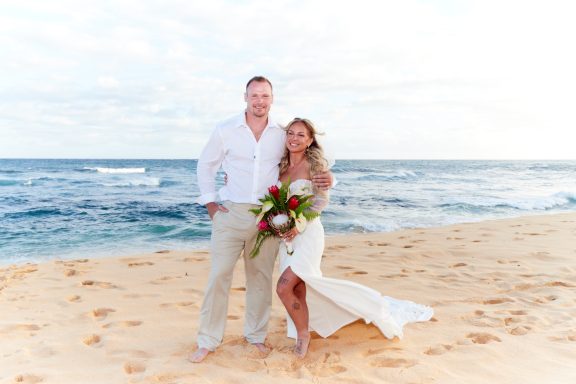 Sandy Beach Wedding Ceremony A couple stands on a beach, with the ocean waves and sandy shore in the background.