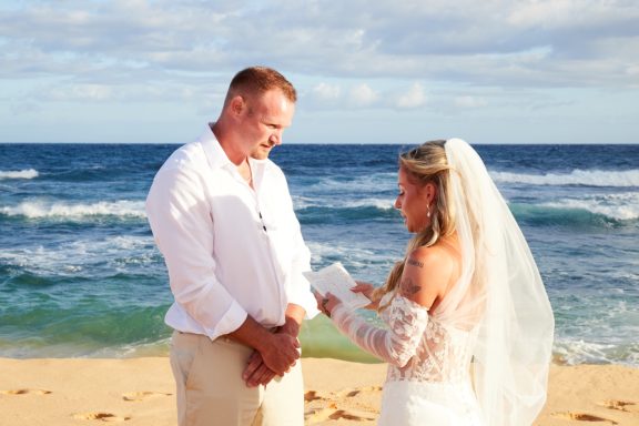 Sandy Beach Wedding Ceremony Bride and groom exchange vows on a beach with ocean waves in the background.