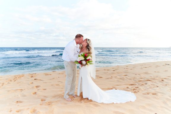 Sandy Beach Wedding Ceremony Couple in wedding attire kissing on a sandy beach with a tropical ocean backdrop.