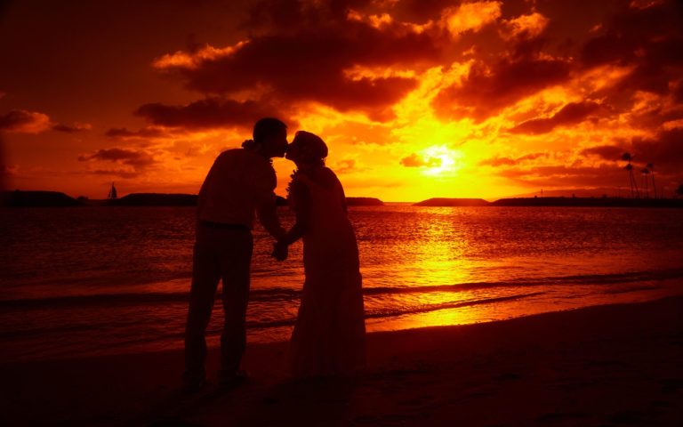 Silhouetted couple embracing at sunset on a beach with vibrant orange skies at Portlock Beach.