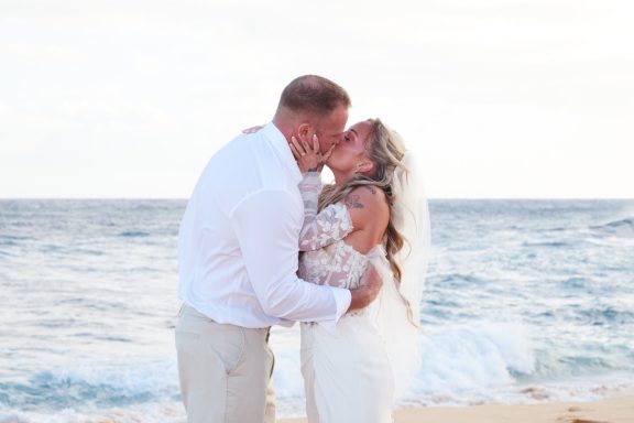 Sandy Beach Wedding Ceremony Bride and groom kissing on the beach with ocean waves in the background.