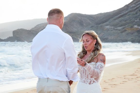 Sandy Beach Wedding Ceremony Couple exchanging vows on a beach during sunset, with mountains in the background.