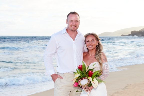 Sandy Beach Wedding Ceremony Couple standing on the beach, smiling, with ocean waves in the background.